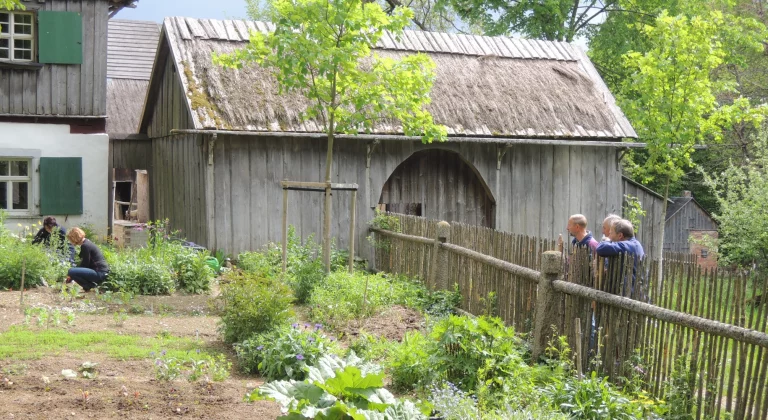 Historisches Hofgut mit Reetdachscheune, Personen besichtigen Garten und Holzzaun