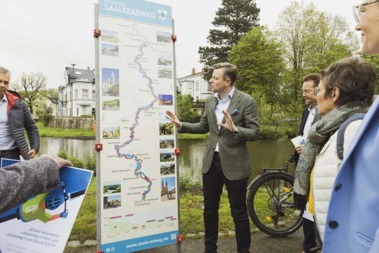 Infotafel zum Saaleradweg am Flussufer, umringt von mehreren Personen im Gespräch