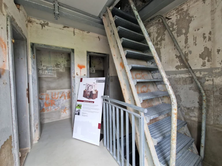 Treppenaufgang und Informationstafel in einem ehemaligen Grenzgebäude mit sichtbarer Verwitterung