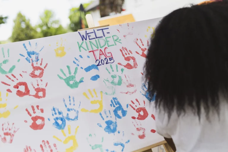 Plakat mit bunten Handabdrücken und Aufschrift Weltkindertag 2025, Person betrachtet das Bild