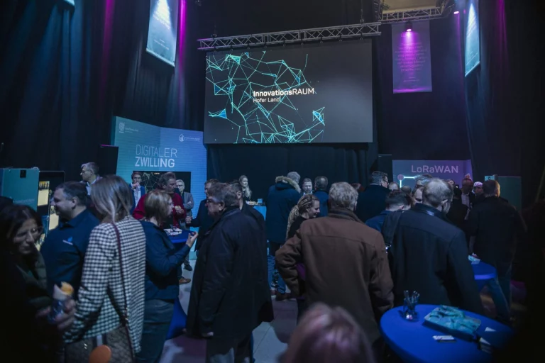 Besucher im abgedunkelten Saal vor Bildschirm mit Schriftzug InnovationsRAUM Hofer Land