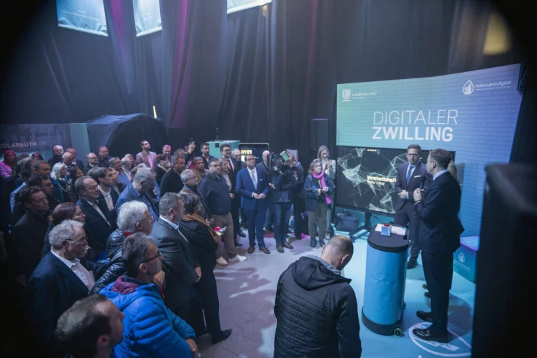 Publikum und Rednerpult vor Bildschirm mit Schriftzug „Digitaler Zwilling“ bei der Eröffnung