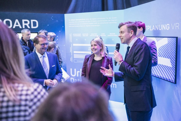 Rednerpult mit Mikrofon vor Publikum und digitaler Standortkarte im Hintergrund