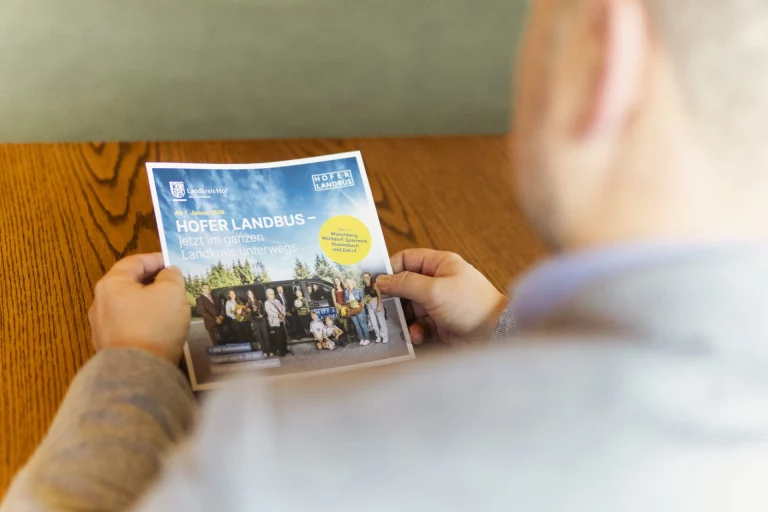 Person betrachtet Flyer zum Hofer LandBus mit Gruppenfoto und Linienhinweisen
