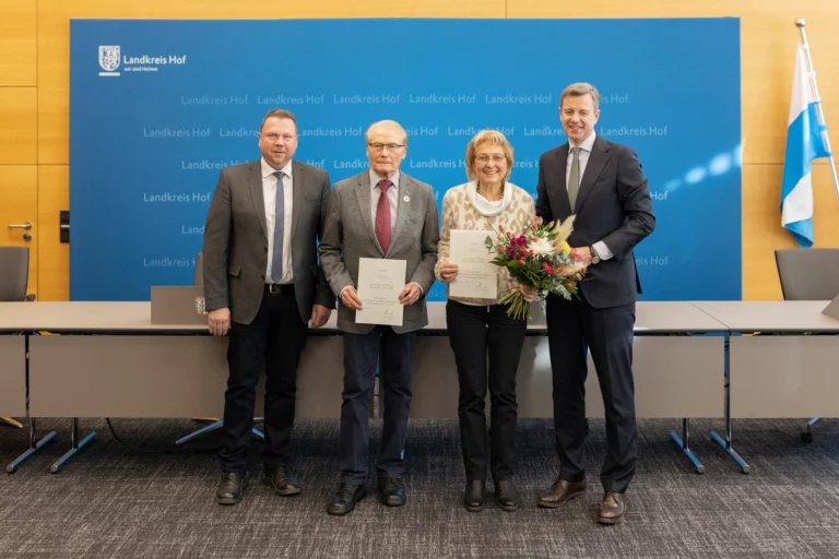 Vier Personen mit Urkunden und Blumenstrauß vor blauer Wand mit Landkreis-Hof-Logo