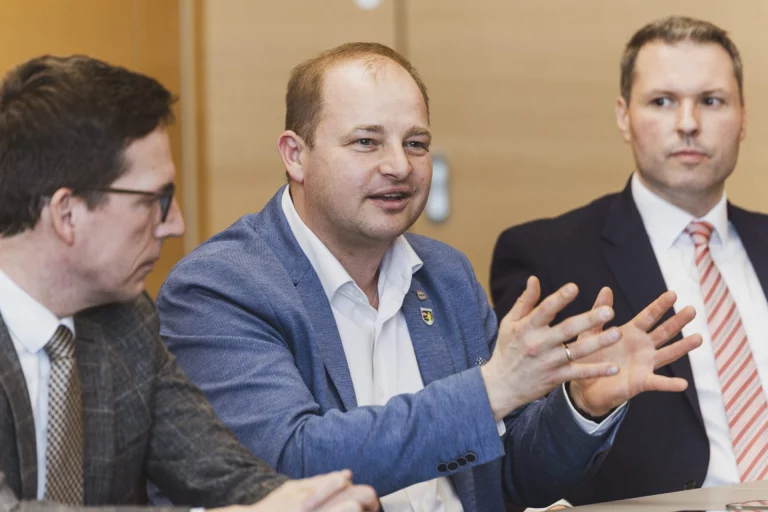 Drei Männer im Gespräch am Tisch, einer gestikulierend während der Vorstellung der Wohnbauoffensive