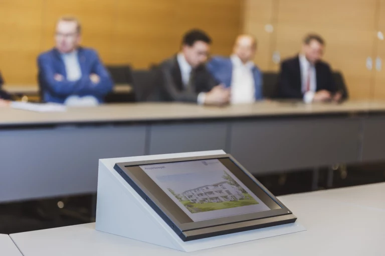Tablet mit Visualisierung eines Wohnbauprojekts, im Hintergrund Männer am Konferenztisch
