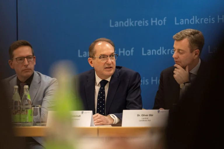 Drei Männer bei Pressekonferenz am Tisch vor Wand mit Schriftzug Landkreis Hof