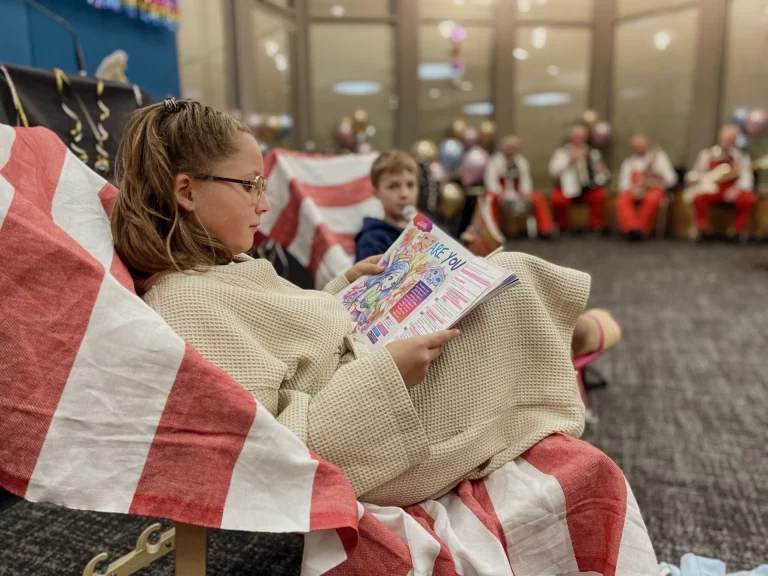 Kinder lesen in Faschingskostümen, im Hintergrund Musikgruppe in roten Kostümen