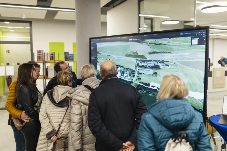Besuchergruppe betrachtet digitale 3D-Luftaufnahme einer Landschaft auf Großbildschirm