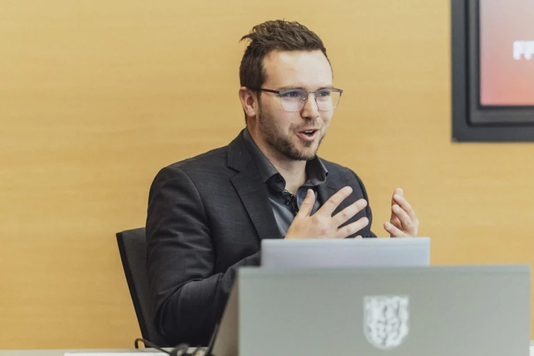 Mann in Sakko spricht gestikulierend hinter einem Laptop mit Landkreiswappen