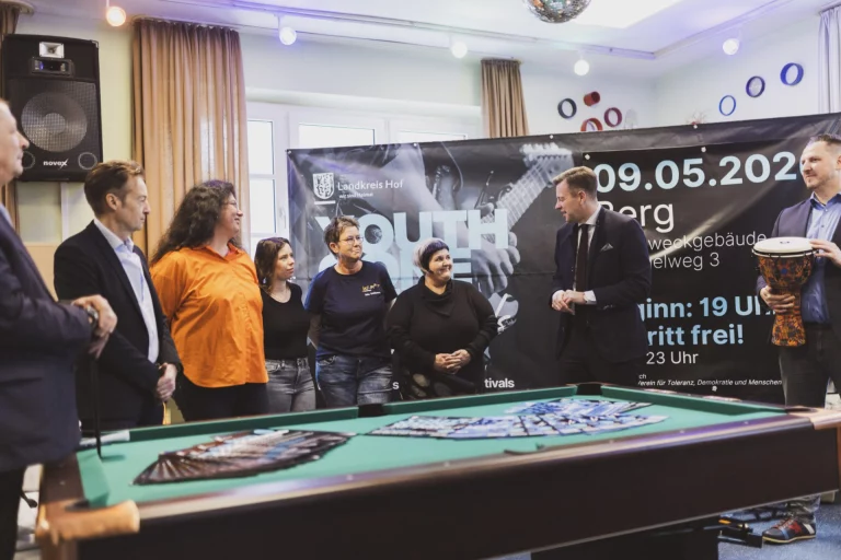 Gruppe von Personen an einem Billardtisch vor Plakat zu den „Youth Gone Wild“-Festivals 2026