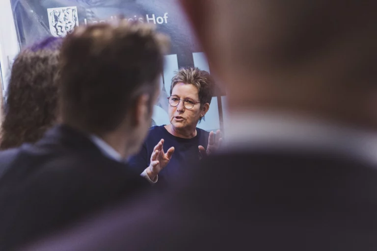 Frau im Gespräch mit zwei Personen vor Banner des Landkreises Hof