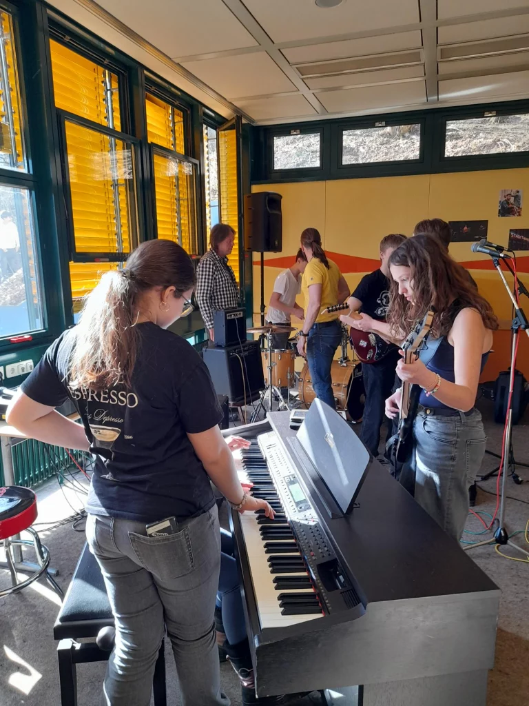 Jugendliche mit E-Gitarren, Keyboard und Schlagzeug proben gemeinsam im Bandraum