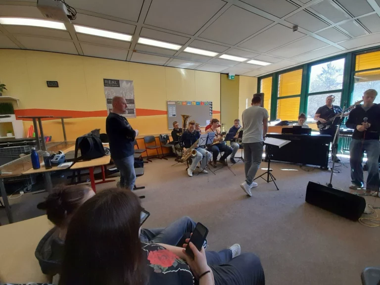 Jugendliche mit Saxophonen und Band proben in Klassenzimmer, Coach im Gespräch mit Trainer