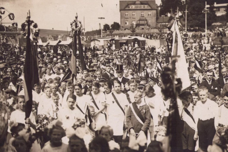 Historische Aufnahme eines Festumzugs mit Fahnenträgern und zahlreichen Teilnehmern bei einem Wiesenfest