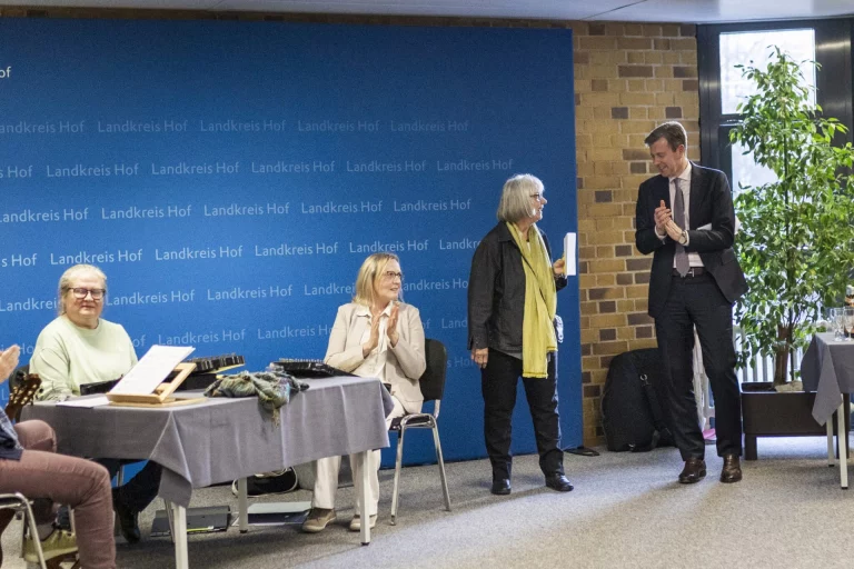 Landrat applaudiert bei Übergabe neben weiteren Personen vor Wand mit „Landkreis Hof“-Schriftzug