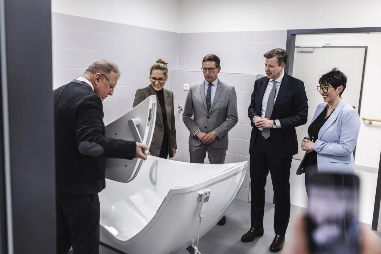 Fünf Personen besichtigen ein Spezial-Pflegebad im neuen Interimsbau der Bezirksklinik Rehau