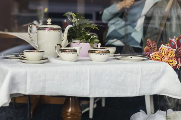 Gedecktes Kaffeegeschirr auf einem Tisch im Schaufenster, im Hintergrund eine Person