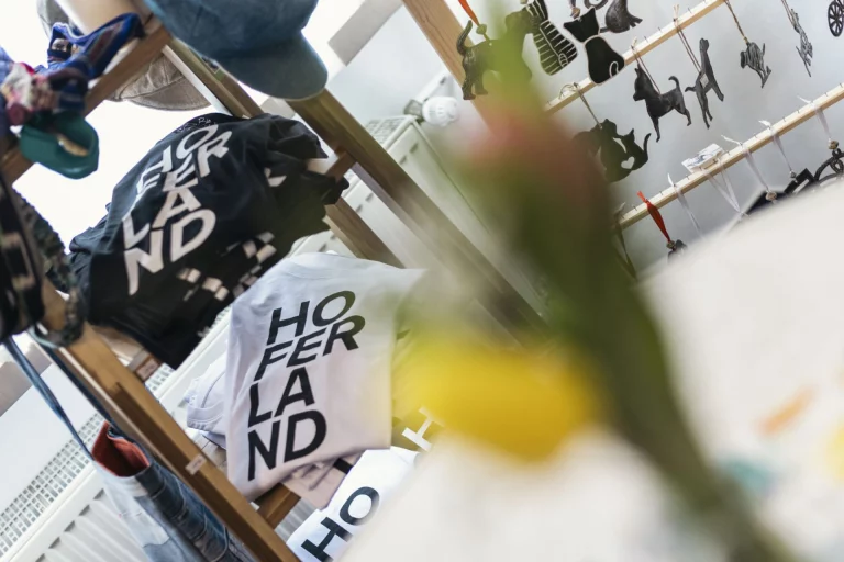 T-Shirts mit Aufschrift „Hoferland“ und Tieranhänger auf einem Verkaufsregal