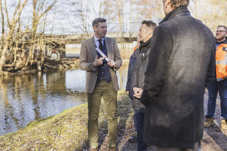 Mann im Sakko spricht mit mehreren Personen am Ufer der Saale nahe einer Brücke