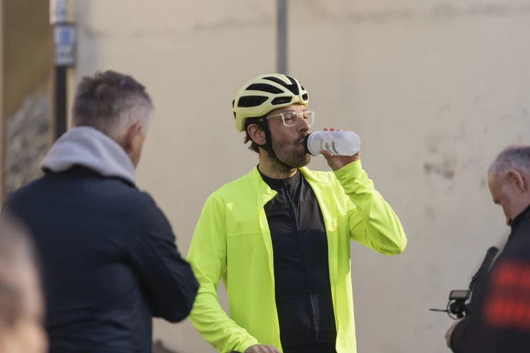 Radfahrer in neongelber Jacke trinkt aus einer Flasche, umgeben von weiteren Personen