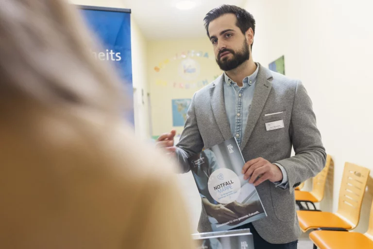 Mann im Flur des Gesundheitsamtes hält Broschüre „Notfallmappe“ in der Hand