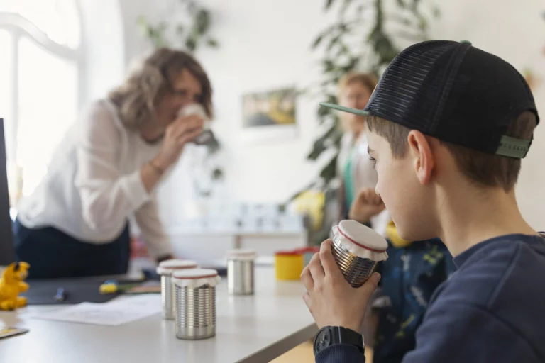 Jugendlicher und weitere Personen hören mit Dosentelefonen bei einer Mitmachaktion des Gesundheitsamtes
