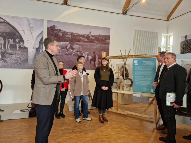 Mann im Sakko erläutert Museumsgruppe historische Aufnahmen und Ausstellungsstücke im Bauernhofmuseum