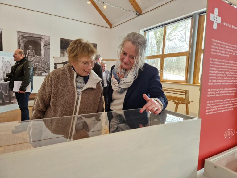 Zwei Frauen betrachten ein Exponat in einer Vitrine vor einer Ausstellungstafel im Museum