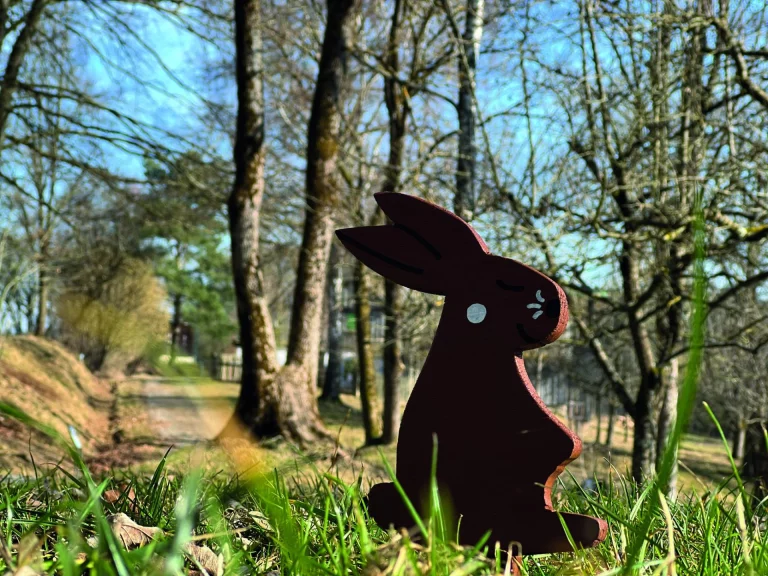 Holzfigur eines Hasen im Gras vor kahlen Bäumen auf dem Museumsgelände
