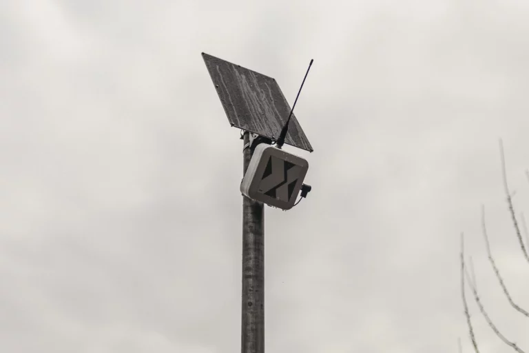 Messgerät mit Solarpanel und Antenne auf Mast an einem Radweg vor bewölktem Himmel