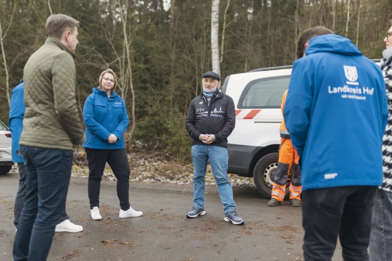 Gruppe von Personen im Gespräch im Wald neben einem Fahrzeug des Landkreises Hof