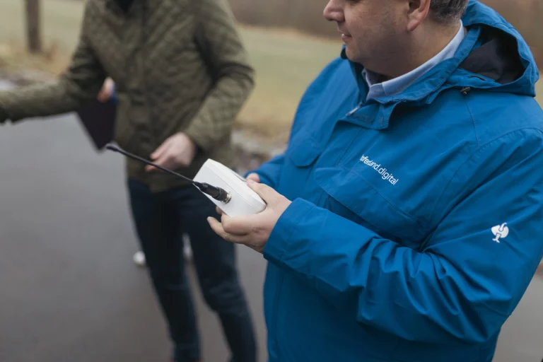 Mann in blauer Jacke hält ein Messgerät mit Antenne an einem Radweg
