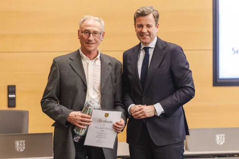 Mann erhält Urkunde und Präsent, daneben Landrat bei der Ehrung im Sitzungssaal