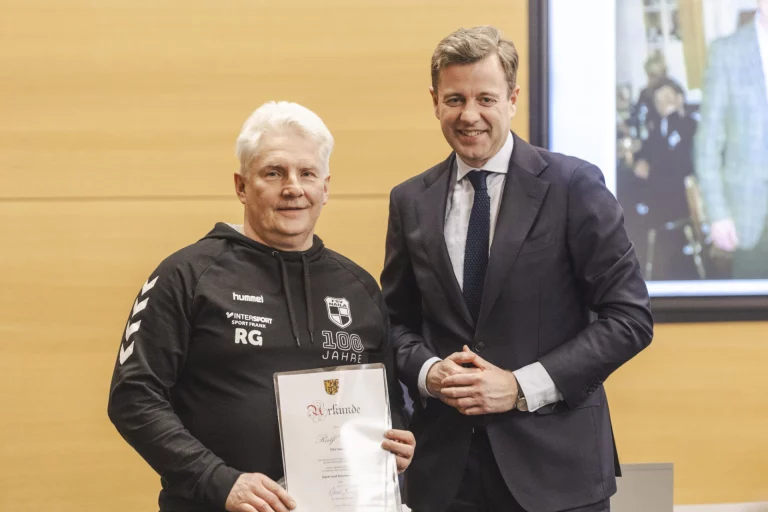 Mann in Sportbekleidung erhält Urkunde von einem Mann im Anzug