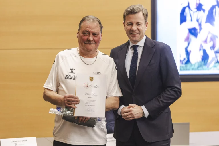 Mann mit Urkunde und Sportshirt neben Landrat bei Ehrung von Vereinsfunktionären