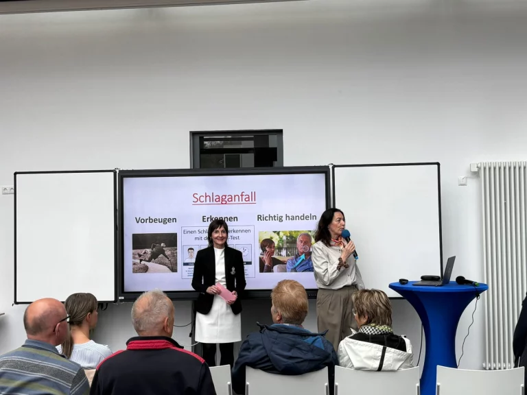 Zwei Frauen bei Vortrag zum Thema Schlaganfall vor sitzendem Publikum