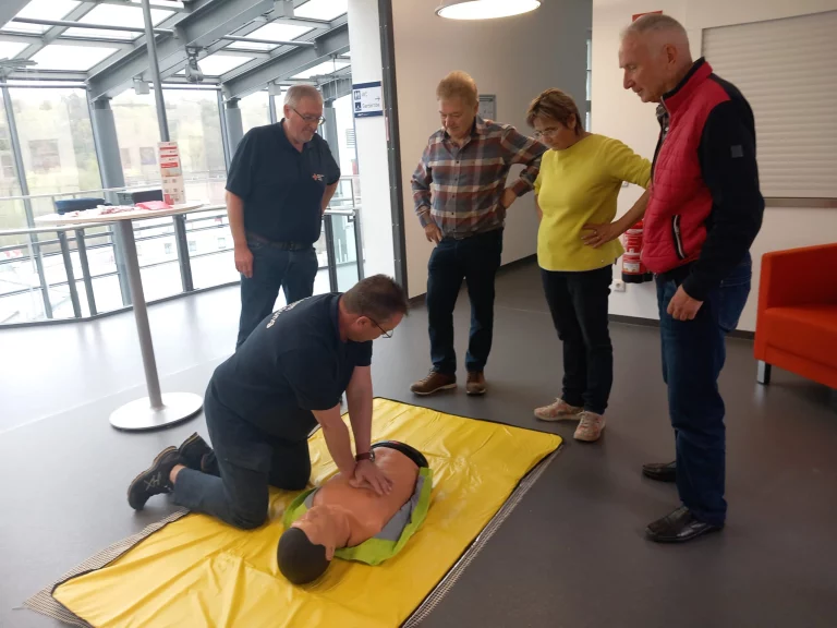 Mann übt Herzdruckmassage an Übungspuppe, vier Personen schauen zu