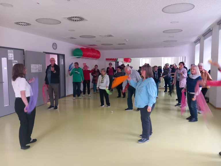 Gruppe von Personen in einem Flur bei einer Bewegungsübung mit bunten Tüchern