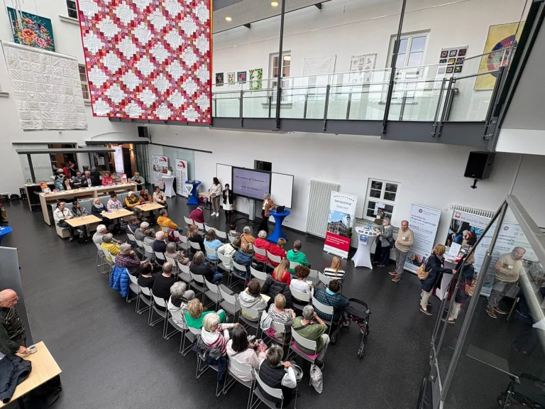 Sitzreihen mit Publikum vor einem Rednerpult in der Halle, Blick von der Empore