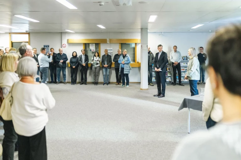 Gäste stehen im Halbkreis bei der Ausstellungseröffnung, im Vordergrund ein kleiner Stehtisch