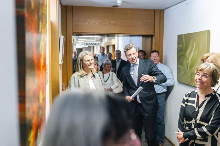 Landrat und Begleitung betreten einen Flur mit ausgestellten Acrylbildern zur Ausstellungseröffnung
