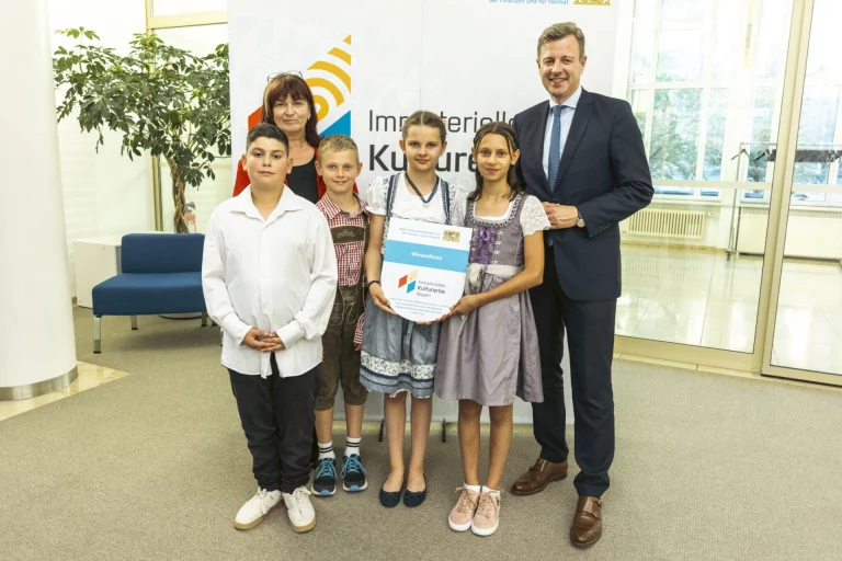 Landrat und vier Kinder in Tracht mit Urkunde vor Banner Immaterielles Kulturerbe