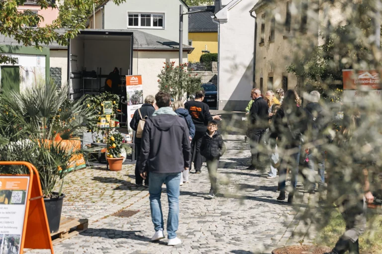 Besucher schlendern an Verkaufsständen mit Pflanzen und einem Infofahrzeug durch eine Gasse