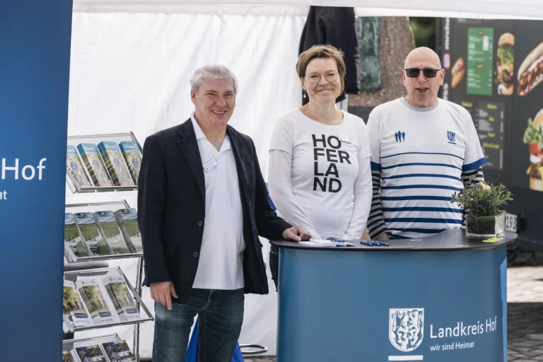Drei Personen am Infostand des Landkreises Hof mit Flyerständer und HofLand-Shirt