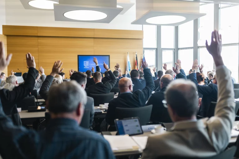Kreistagsmitglieder heben bei einer Abstimmung im Sitzungssaal die Hand