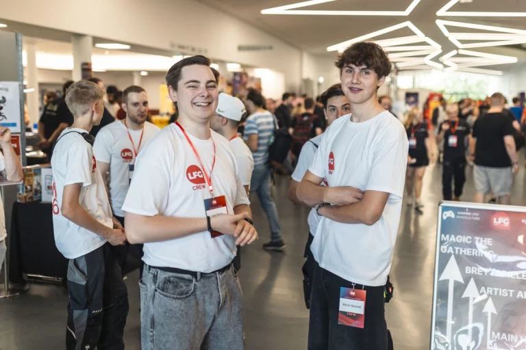 Zwei lächelnde Crewmitglieder in weißen LFG-Shirts in der Messehalle der LFG Con