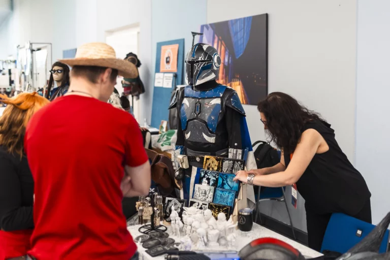 Messestand mit Mandalorianer-Kostüm, 3D-gedruckten Figuren und Merchandise, Besucher im Gespräch mit Ausstellerin
