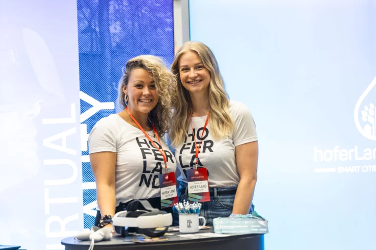Zwei Frauen im hoferLand-Shirt an einem Messestand mit VR-Brille vor der LFG Con